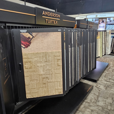 Display of Anderson Tuftex carpet samples with beige and golden patterns, branding prominently visible on black stands in a well-lit showroom.